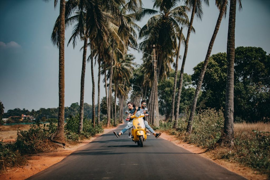 A joyful couple rides a yellow scooter through a scenic palm-lined road, capturing the essence of tropical travel and adventure.